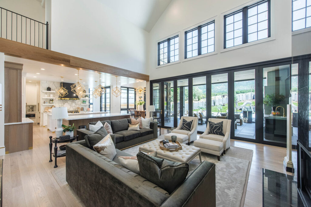 Fully furnished home showcasing Andersen 200 Series windows and doors. There's a brightly lit kitchen in the back left corner, two grey couches, two white chairs and a coffee table in front of the backyard wall covered with Andersen windows.